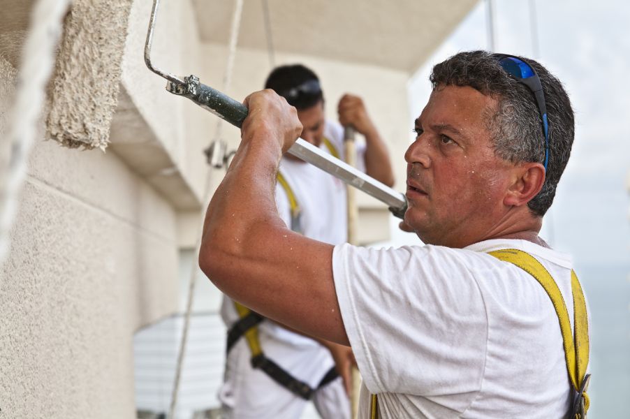 Professional painting contractor applying exterior coating using commercial-grade paint and tools